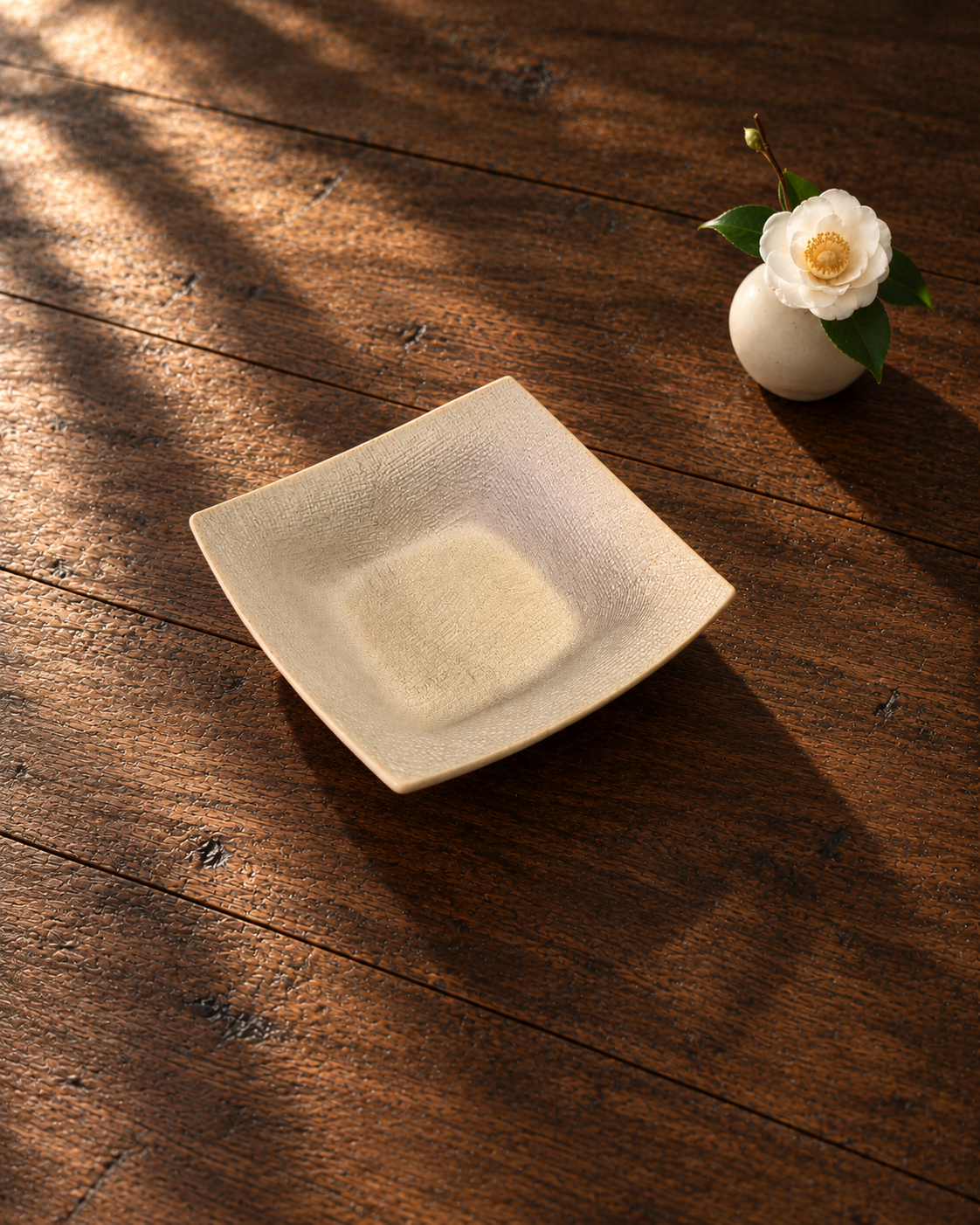 Plat carré Sable tissé OrienX sur une table en bois avec une fleur blanche